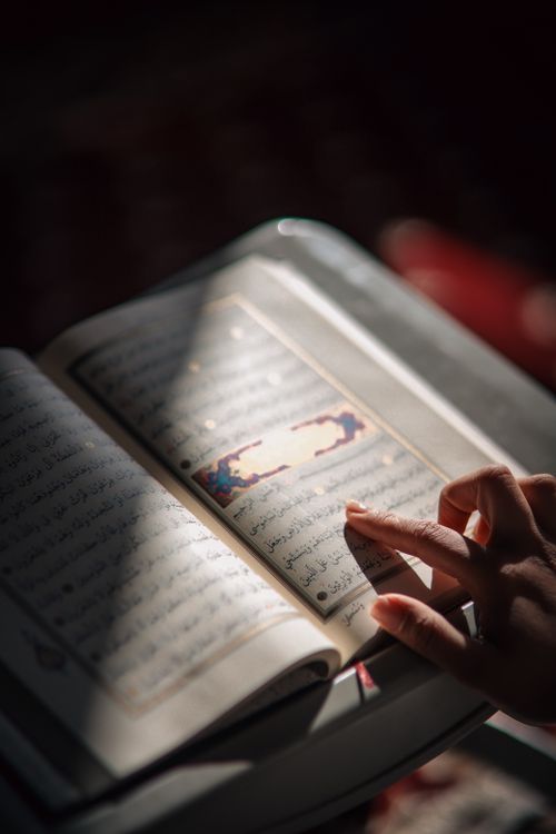 Photograph of a hand resting on an open printed Mushaf